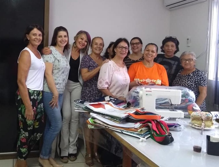 As professoras Carmem Cardoso e Ionara Pizzutti recebem as sacolas de banner confeccionadas pela equipe do projeto RElona.